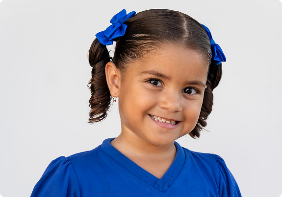 Menina sorridente com laços azuis no cabelo, uniforme do Centro de Estudos
